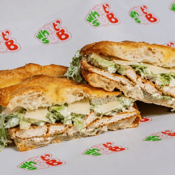 Two halves of a crispy chicken Caesar sub sandwich on branded What's Up paper.