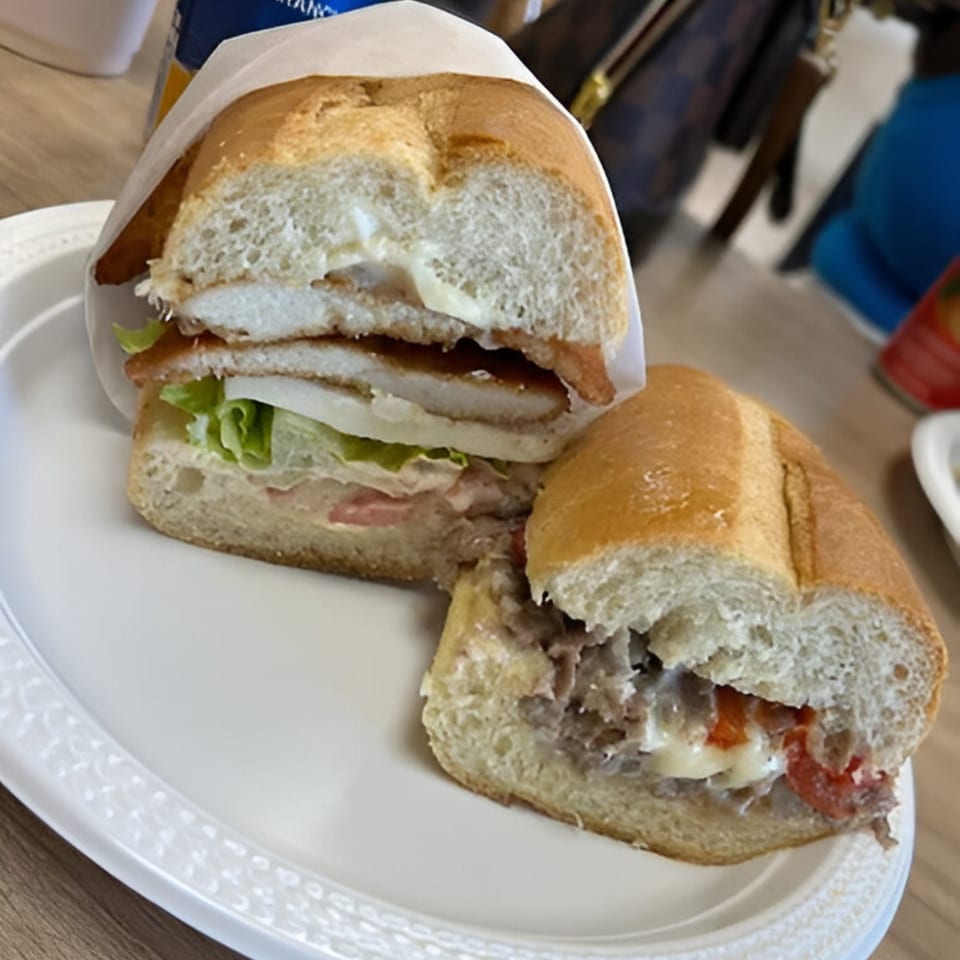 Two Italian subs on a white plate, one with chicken cutlet, the other with steak and cheese.