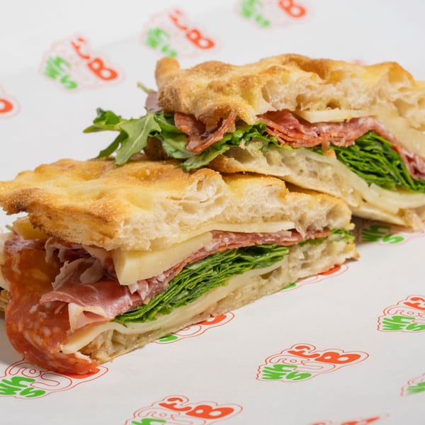 Two halves of an Italian sub on focaccia bread, filled with salami, cheese, and greens.