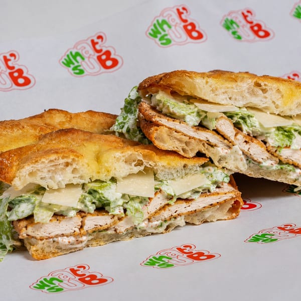Two halves of a What's Sub chicken Caesar sandwich on branded parchment paper.
