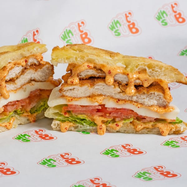 A chicken sandwich cut in half, revealing crispy chicken, melted cheese, lettuce, tomato, and sauce.