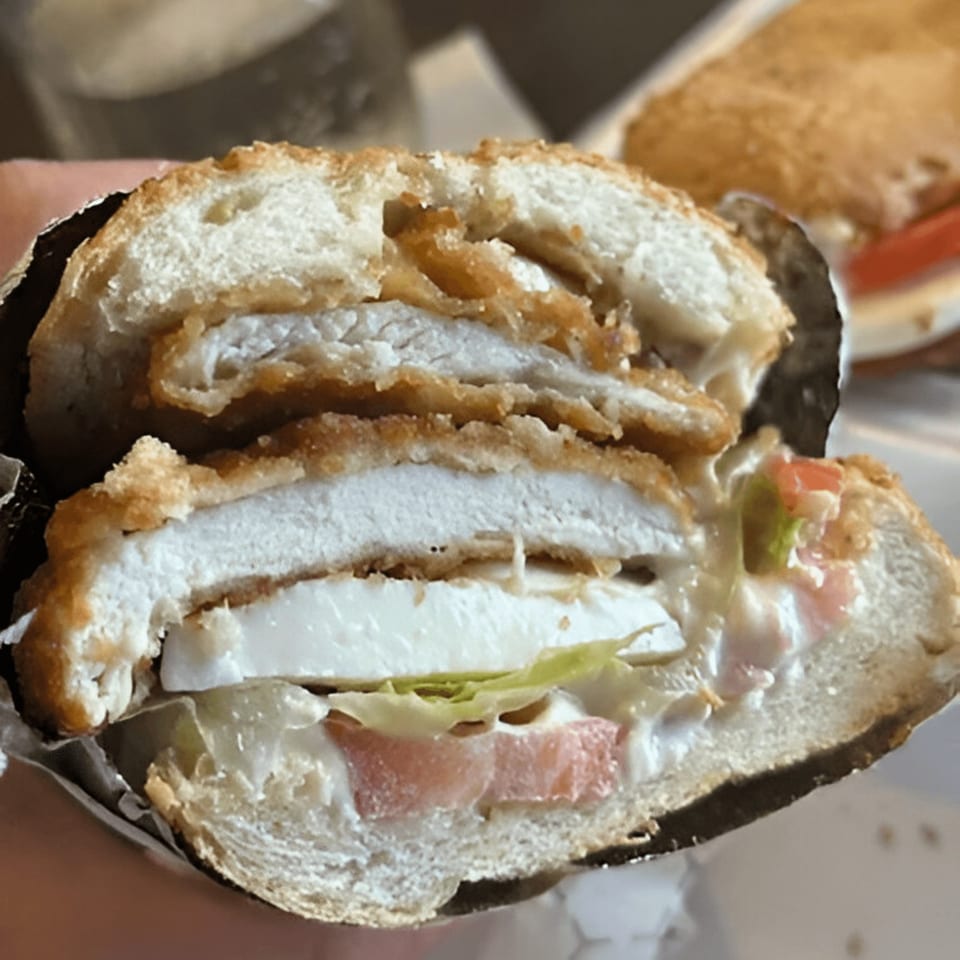 A close-up of a WhatSub Sub Shop Italian sub, cut in half, revealing crispy chicken, cheese, and vegetables.
