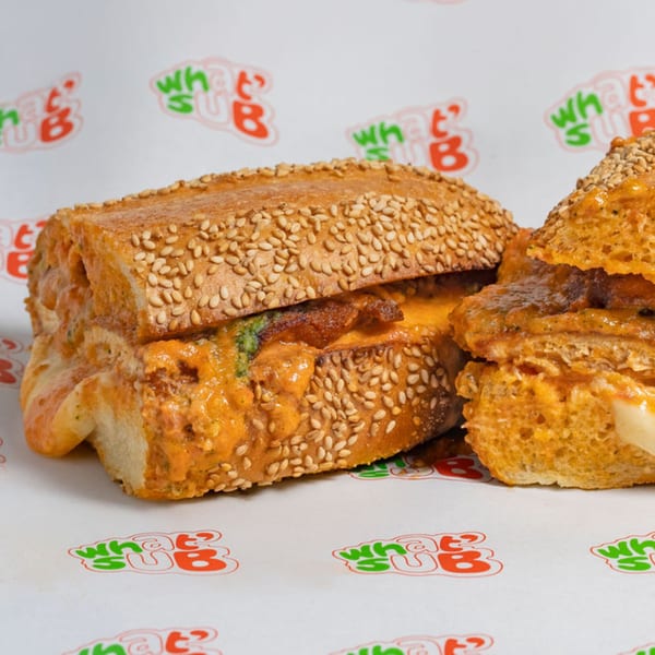 Two halves of a WhatSub Italian sub sandwich with melted cheese and meat on branded paper.
