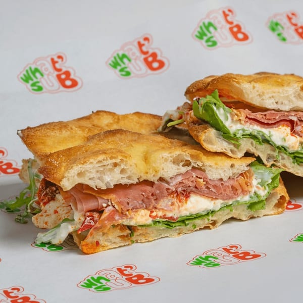 Two halves of a What a Sub sandwich filled with meat, cheese, and lettuce on branded paper.