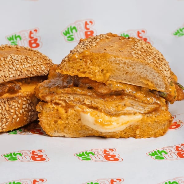 Two What's Up subs with chicken, melted cheese, and sauce on sesame seed buns.