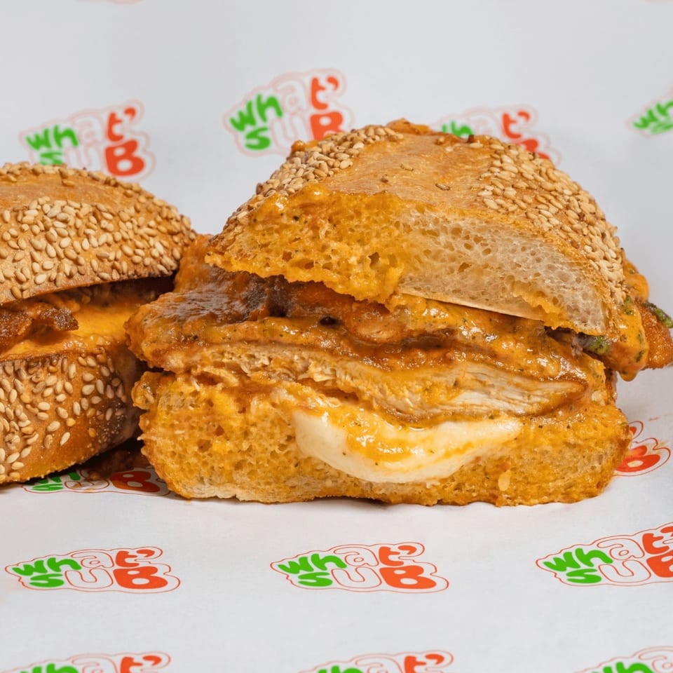 Two What's Up subs with chicken, melted cheese, and sauce on sesame seed buns.
