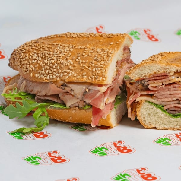 A sliced What a Sub sandwich with meat, cheese, and arugula on a sesame seed bun.