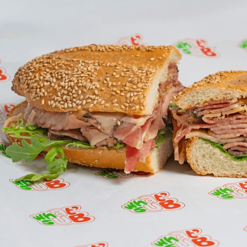A sliced What a Sub sandwich with meat, cheese, and arugula on a sesame seed bun.