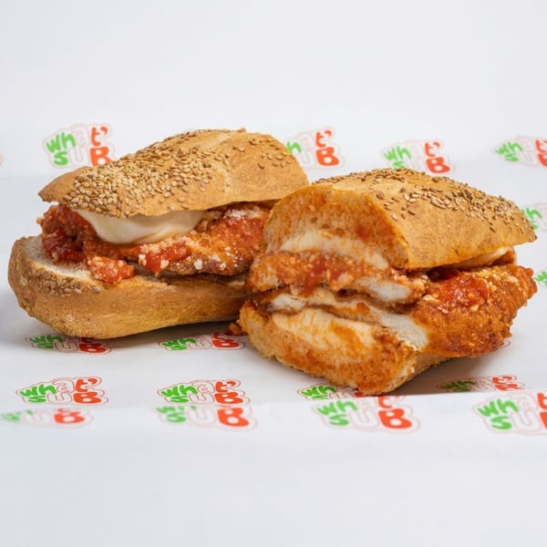 Two chicken parmesan subs with melted mozzarella and marinara sauce on sesame seed rolls.