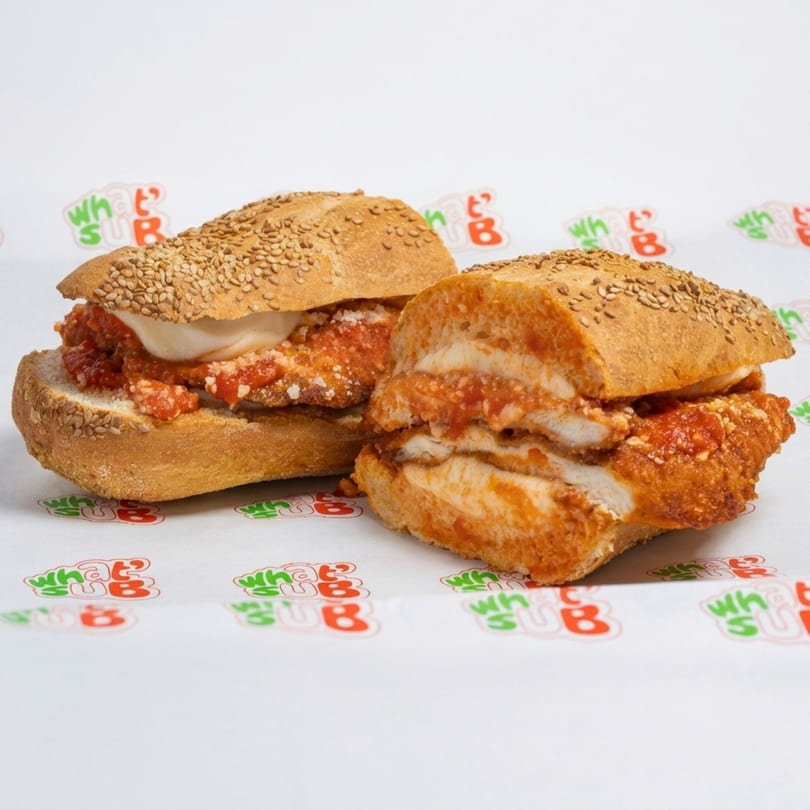 Two chicken parmesan subs with melted mozzarella and marinara sauce on sesame seed rolls.