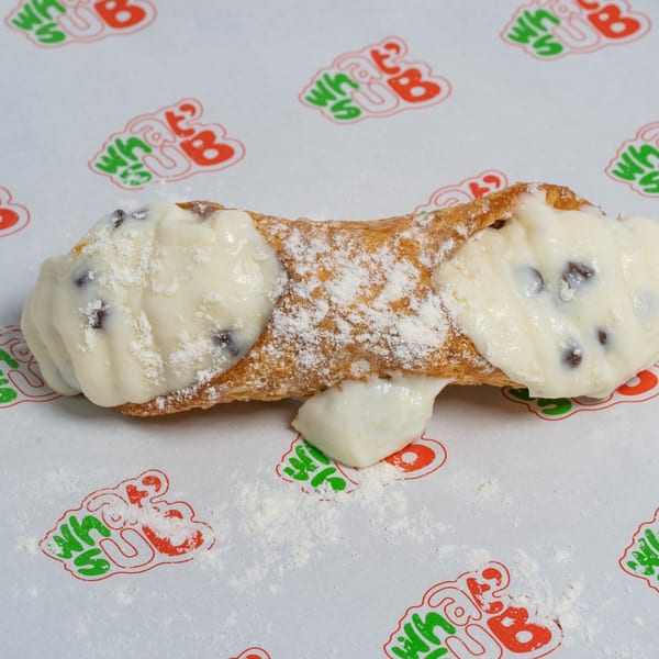 A single cannoli filled with white cream and chocolate chips, dusted with powdered sugar.