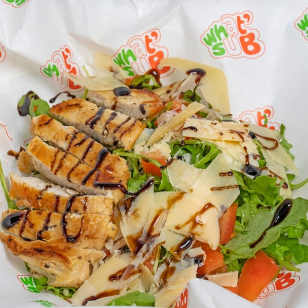 Grilled chicken salad with arugula, tomatoes, parmesan, and balsamic glaze in What's Up branded paper.