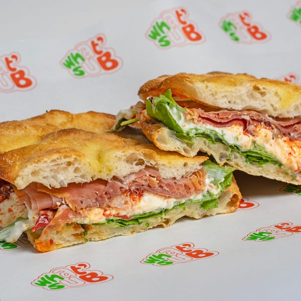 Two halves of a WhatSub Italian sub sandwich with ham, lettuce, and creamy sauce.