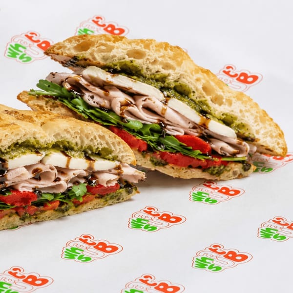 Two halves of a sandwich with turkey, mozzarella, pesto, arugula, and roasted red peppers.