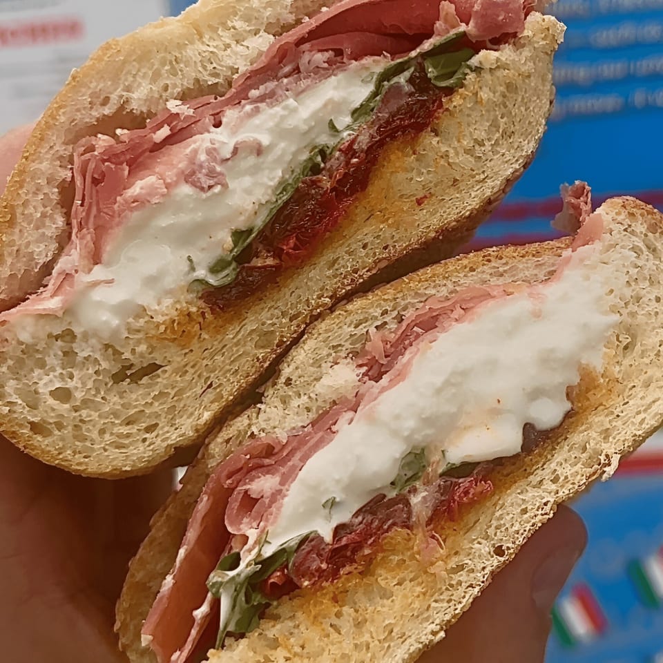 A sliced Italian sub sandwich with prosciutto, mozzarella, arugula, and sun-dried tomatoes.