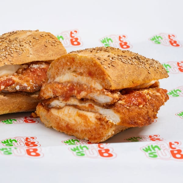 Two chicken parmesan subs with red sauce and cheese on sesame seed buns, on WhatSub branded paper.