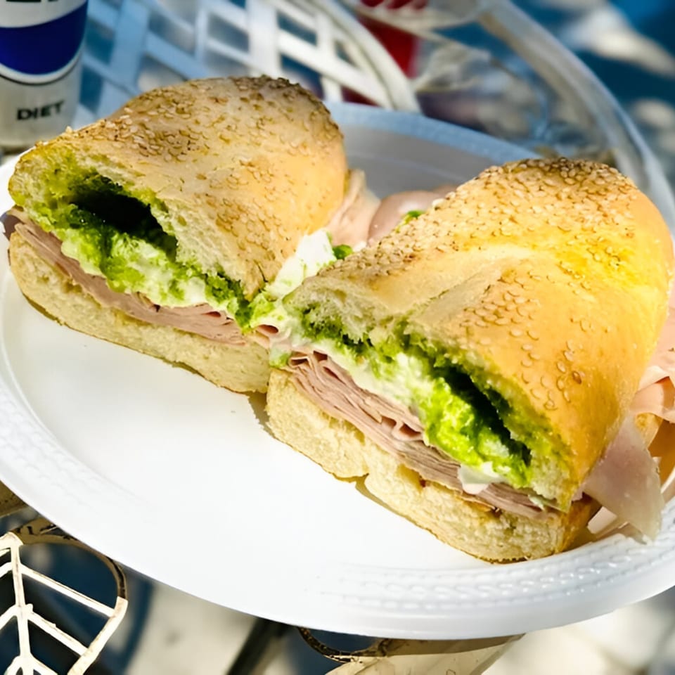 A sliced Italian sub sandwich with pesto, meat, and cheese on a white plate.