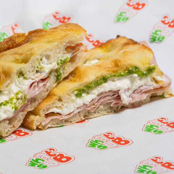 WhatSub Sub Shop's Italian focaccia sandwich with ham, creamy cheese, and pesto on branded paper.