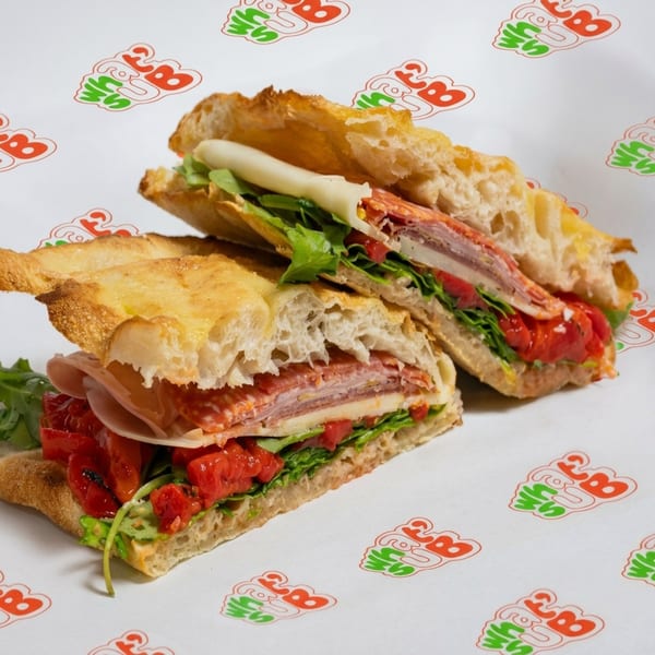 Two halves of a focaccia sandwich filled with deli meats, cheese, arugula, and roasted red peppers.