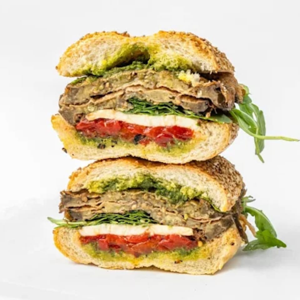 A sliced Italian sub sandwich with pesto, roasted red peppers, mozzarella, and eggplant on a white background.