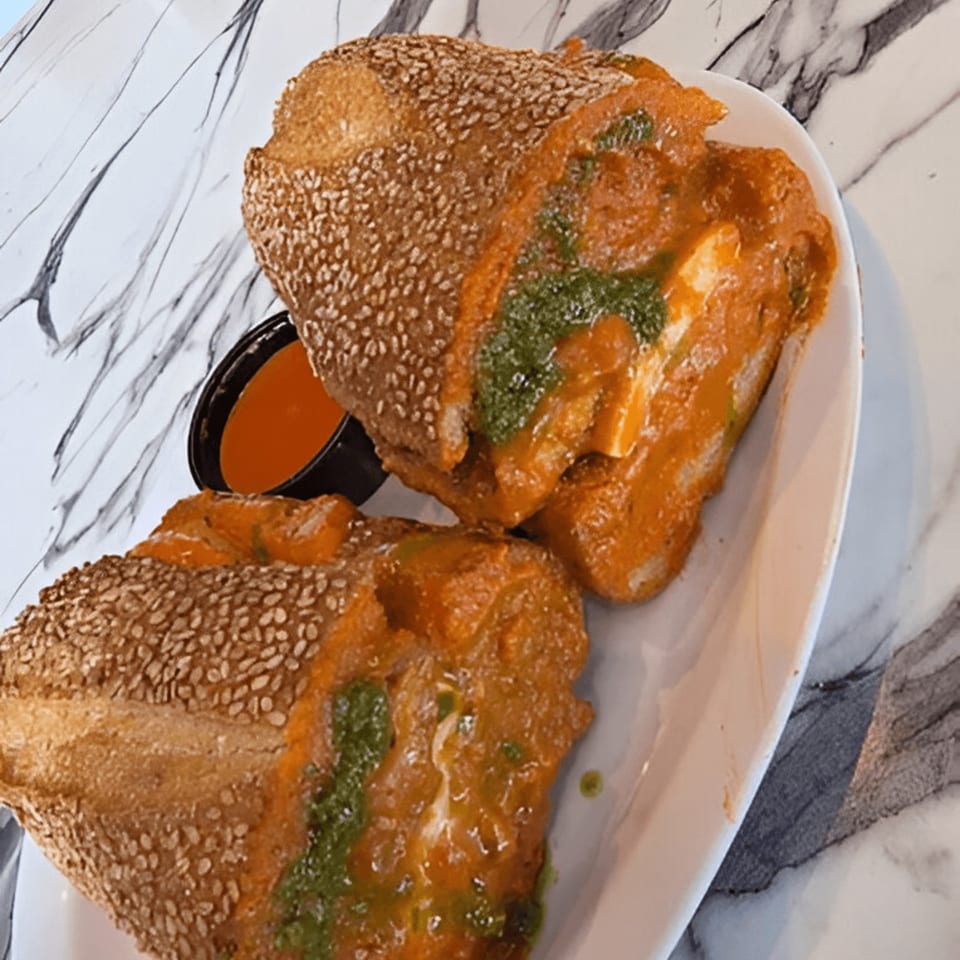 Two halves of a sesame seed sub roll filled with red sauce, cheese, and green pesto.