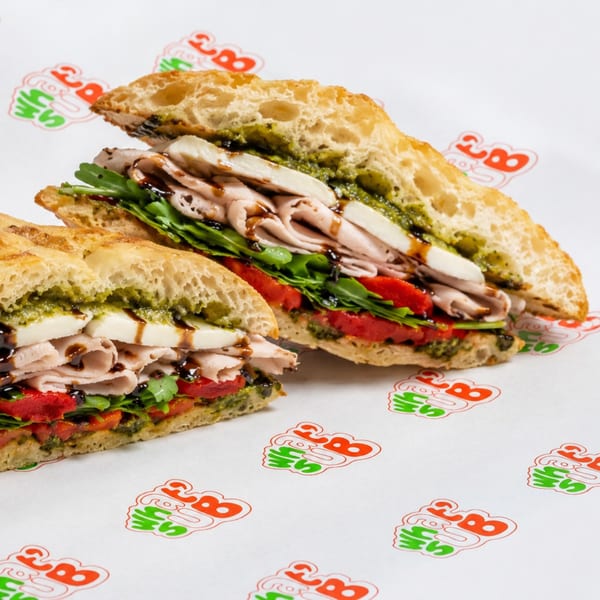 Two halves of a sandwich with turkey, mozzarella, pesto, arugula, and roasted red peppers.