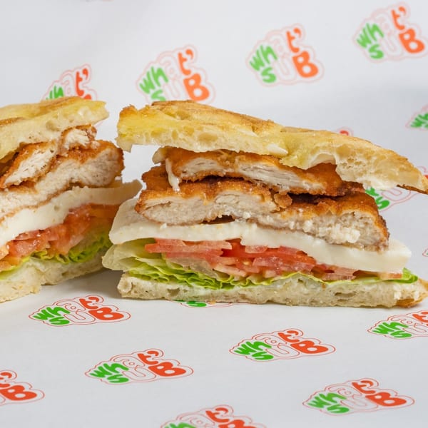 Two halves of a crispy chicken sandwich with lettuce, tomato, and cheese on focaccia bread.